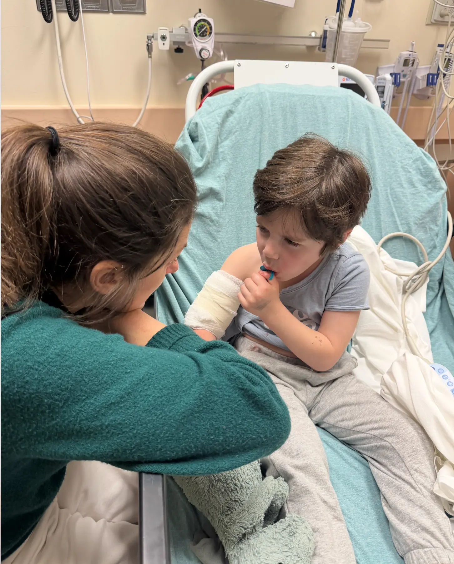 A parent comforting a young child with a bandaged arm in an emergency room