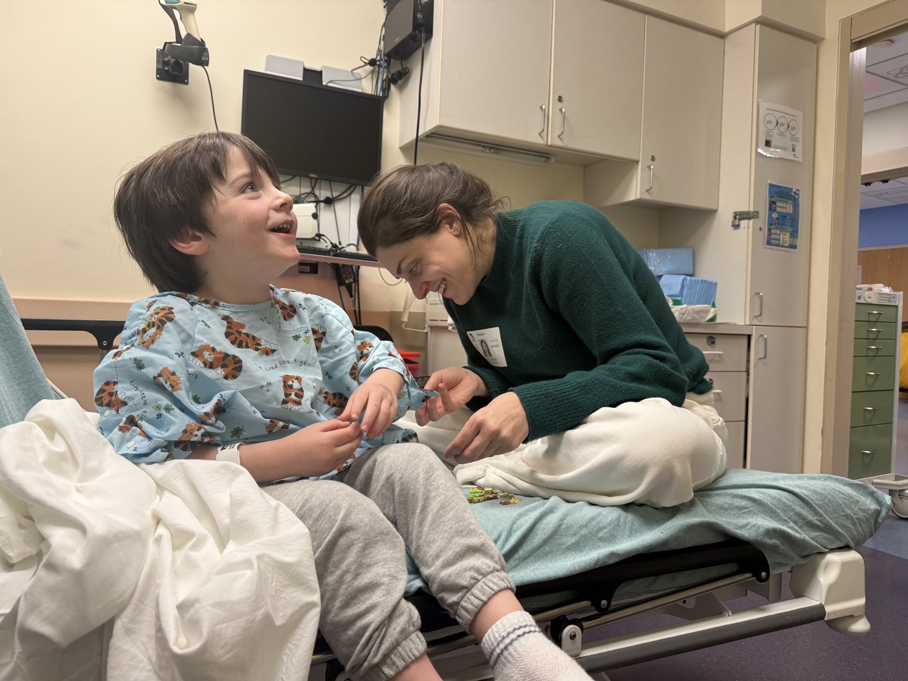 A child smiling with a caregiver at their bedside